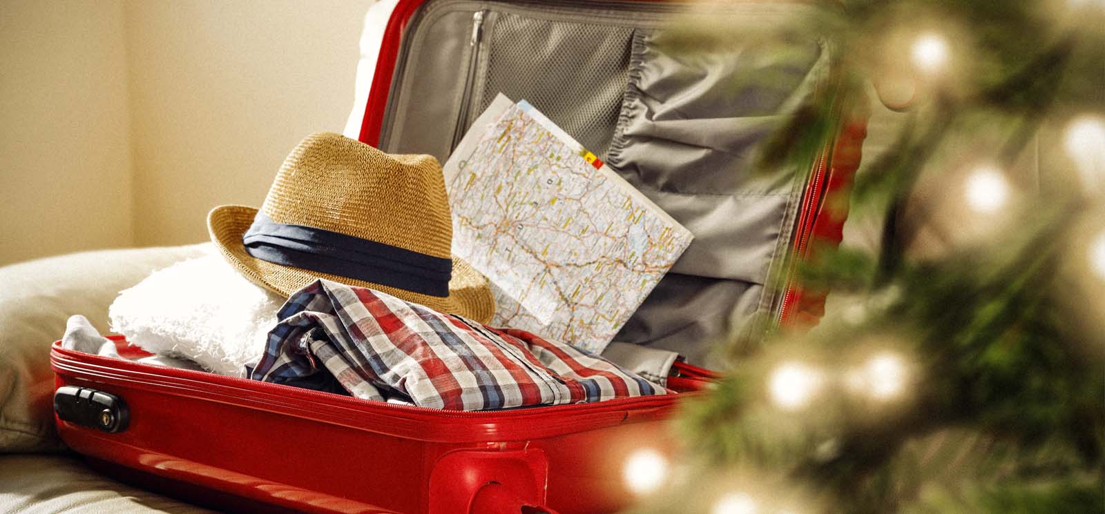 red suitcase containing hat, clothes, and map. Christmas tree in the foreground.
